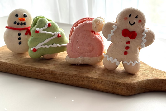 Four Christmas-themed Macaron cookies on a wooden board with a white curtain background